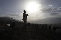 Afghan men pray near the grave of their relatives killed in bombings near Syed Al-Shahada School